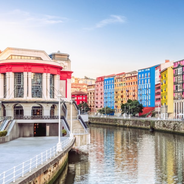 Der Mercado de la Ribera in Bilbao am linken Ufer eines Flusses, auf der anderen Flussseite befinden sich weitere bunte Häuser.