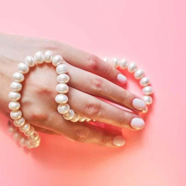Eine Frauenhand mit Perlenkette umwickelt auf rosa Untergrund