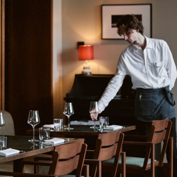 Ein junger Mann richtet ein Glas auf einem gedeckten Tisch in einem stilvollen Restaurant.