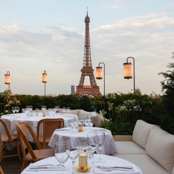 Dachterrasse eines Restaurants mit weiß eingedeckten Tischen vor dem Eiffelturm.
