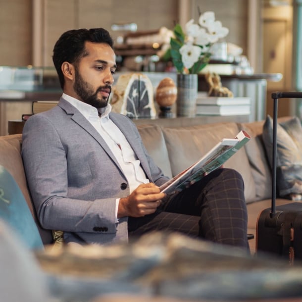 Ein elegant gekleideter Mann liest eine Zeitschrift auf einem Sofa in einer Flughafenlounge.