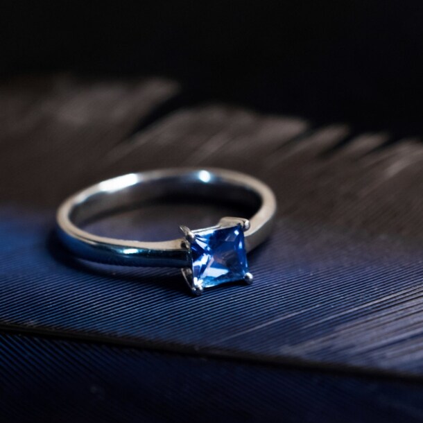 Ein Silberring mit blauem Edelstein auf einer schwarzen Feder.