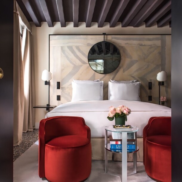 Stilvolles Hotelzimmer mit Doppelbett, im Vordergrund eine geöffnete Flügeltür mit goldenen Türklinken.