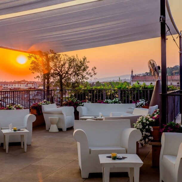 Dachterrasse mit weißen Sitzmöbeln in urbaner, mediterraner Umgebung bei Sonnenuntergang.
