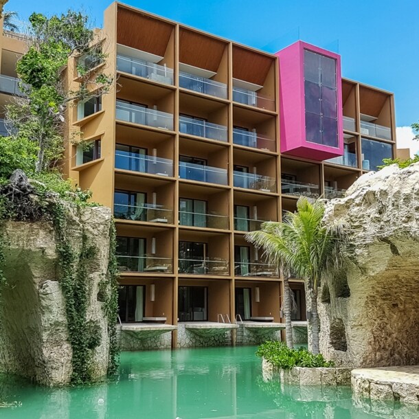 Moderner Hotelkomplex, umgeben von bepflanzten Felsen an einem Pool mit türkisfarbenem Wasser.