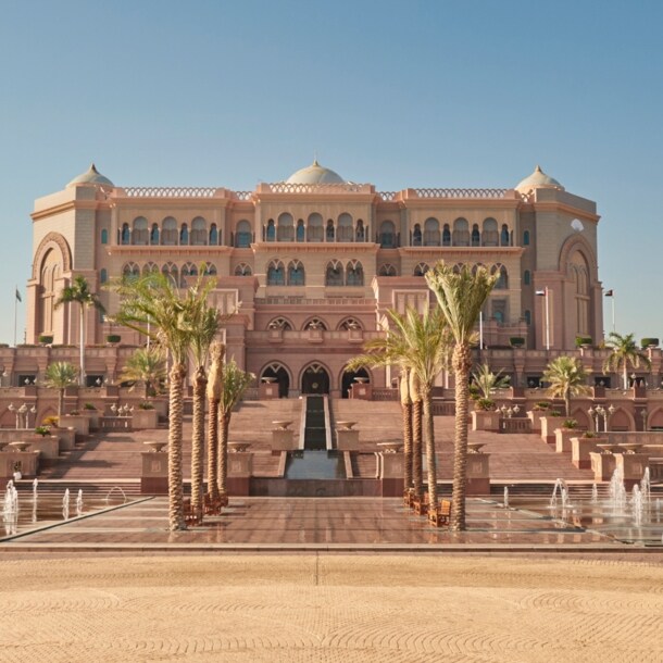 Außenansicht des Emirates Palace Mandarin Oriental Hotels in Abu Dhabi mit Palmen und Brunnen im Vordergrund.