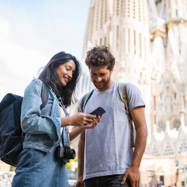 Zwei Personen stehen in Barcelona vor der Sagrada Família und blicken zusammen auf ein Smartphone.