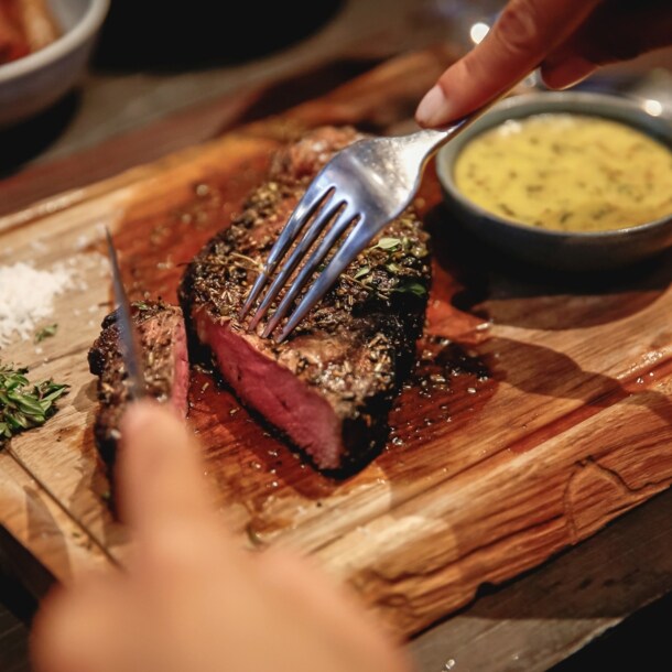 Nahaufnahme eines angeschnittenen Steaks auf einem Holzbrett neben einer Schale mit Soße.