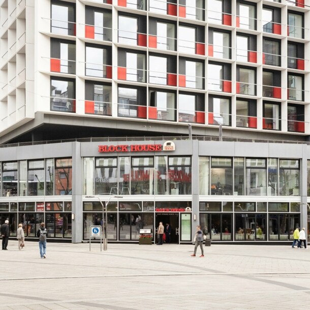 Personen am Eingang einer Block House Filiale in einem grauen Neubau in einer Fußgängerzone in Innenstadtlage.