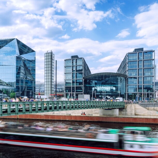 Modernes Bauensemble des Berliner Hauptbahnhofes mit Glasfassade am Flussufer, im Vordergrund ein Ausflugsboot in Unschärfe.