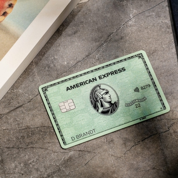 ine grüne American Express Kreditkarte liegt auf einem grauen Marmortisch neben einem Buch.