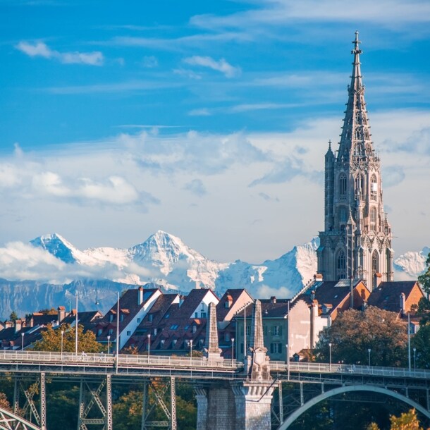 Turm der Kathedrale von Bern mit schneebedeckten Gipfeln im Hintergrund.