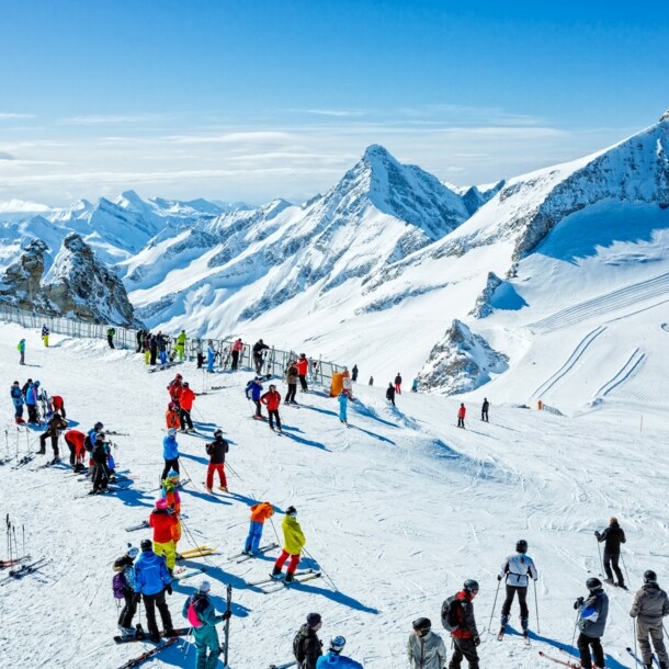 Skifahrende auf einem Plateau auf einer Skipiste vor schneebedecktem Gipfelpanorama.