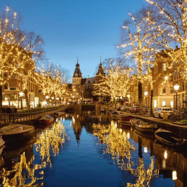 Gracht mit von Lichterketten beleuchteten Bäumen am Abend.