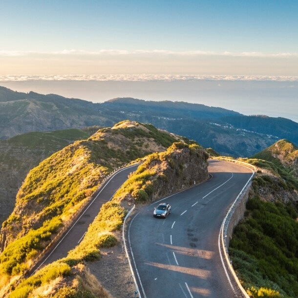 Ein Auto auf einer kurvigen Straße durch eine hügelige Landschaft auf Madeira.