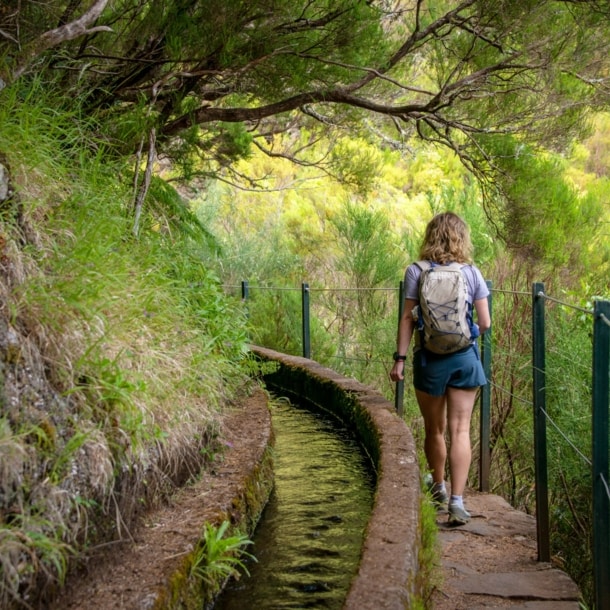 Rückansicht einer Frau auf einem Wanderweg auf Madeira, der entlang eines Bewässerungskanals verläuft.