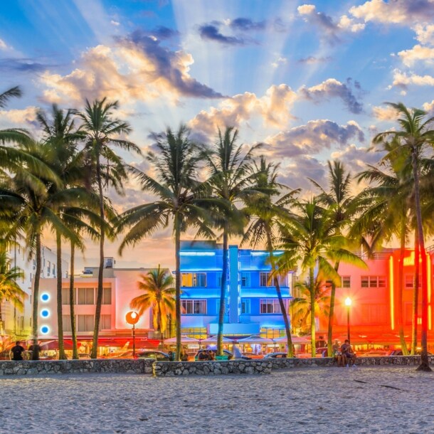 Strandpromenade mit Palmen und Art-déco-Gebäuden mit Neon-Beleuchtung am Abend.