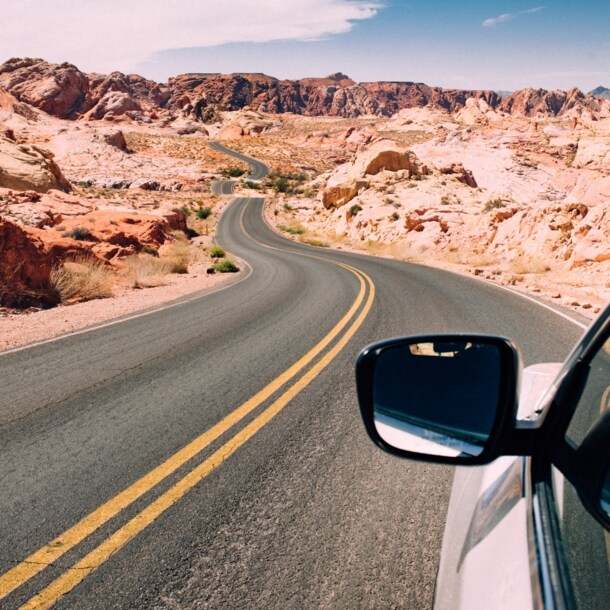 Seitenspiegel eines Autos auf einer US-amerikanischen Autobahn in einer felsigen Wüstenlandschaft.