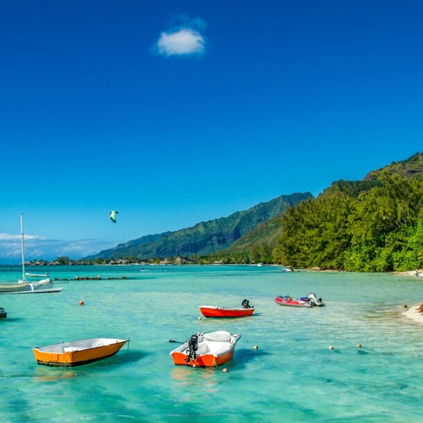 Kleine Boote im türkisblauen Wasser an einem Sandstrand mit tropischer Vegetation.