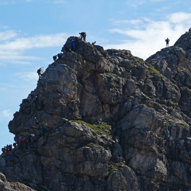 Mehrere Personen, die einen Felsen am Hindelanger Klettersteig erklimmen.