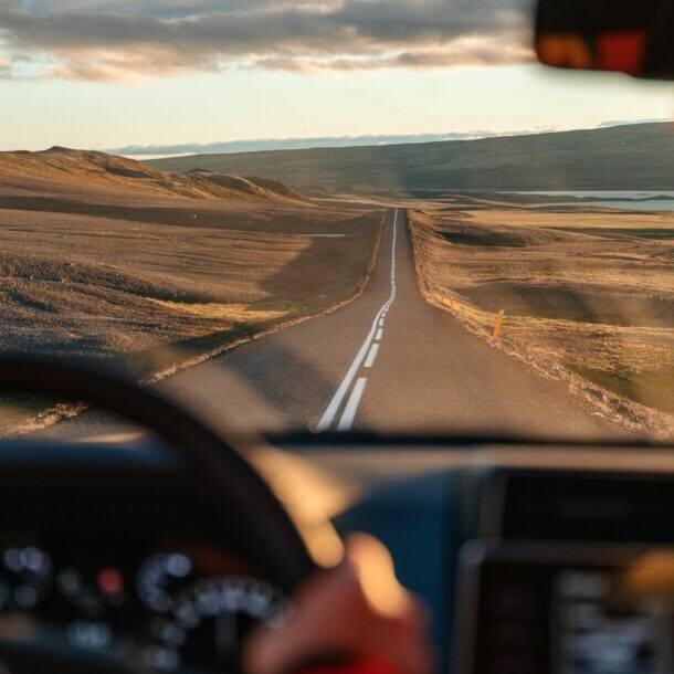 Blick auf eine Landstraße in karger, hügeliger Naturlandschaft durch die Windschutzscheibe eines fahrenden Autos.