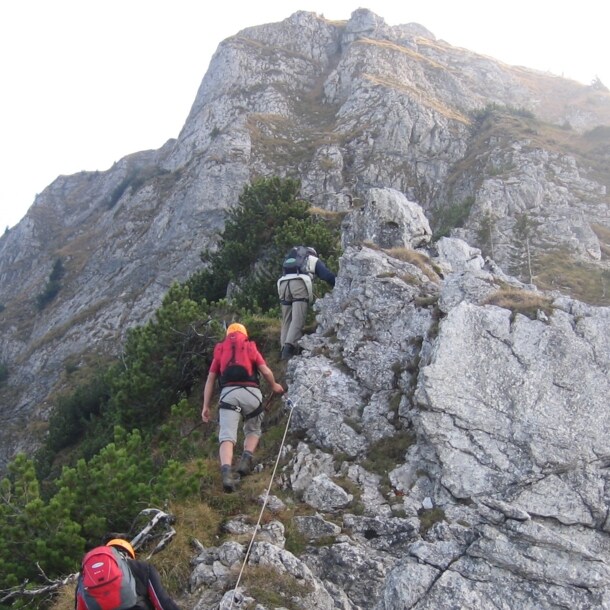 Drei Personen in Kletterausrüstung an einem Felsen an einem der Tegelberger Klettersteige.