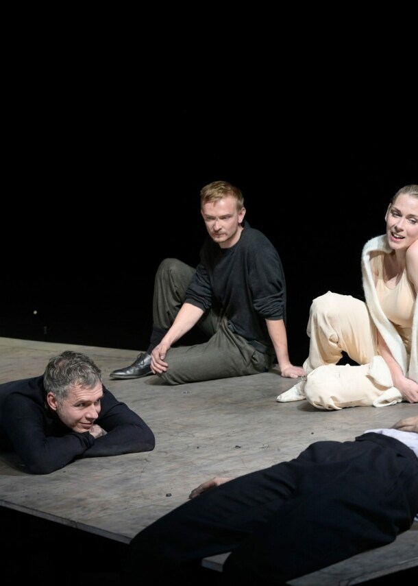 Zwei Männer und zwei Frauen sitzen oder liegen auf einer Bühne aus Betonun vor schwarzem Hintergrund