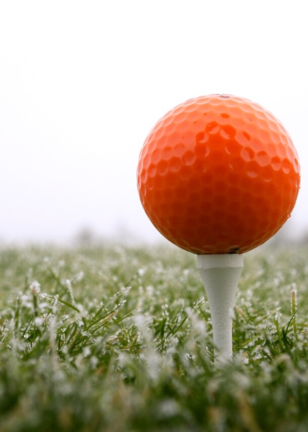Ein roter Golfball auf dem Tee, darunter taubedeckter Rasen