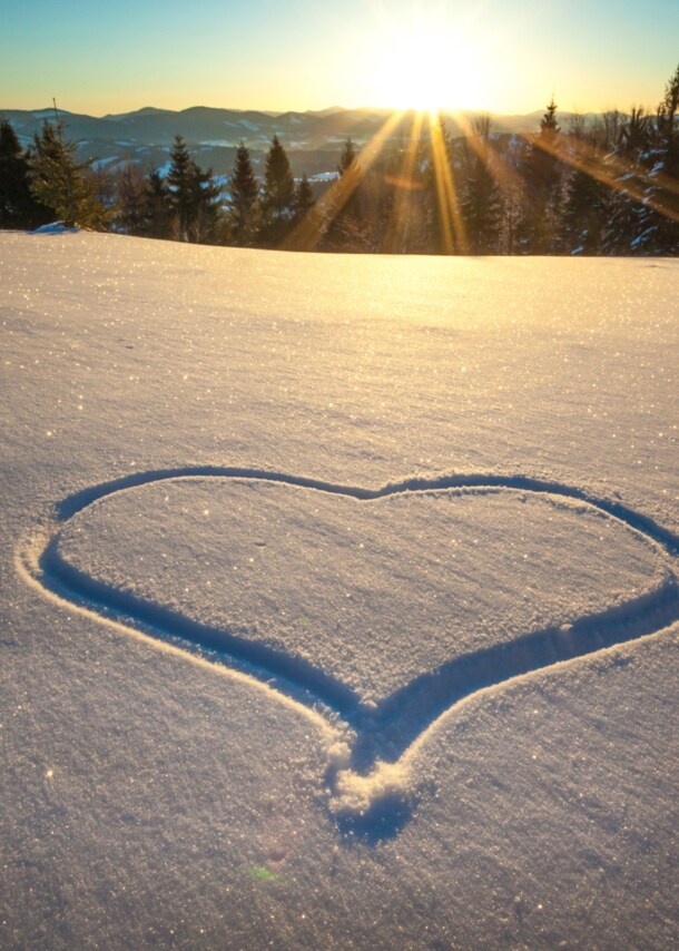 Ein Herz in den Schnee gezeichnet, im Hintergrund ein Wald und Berge