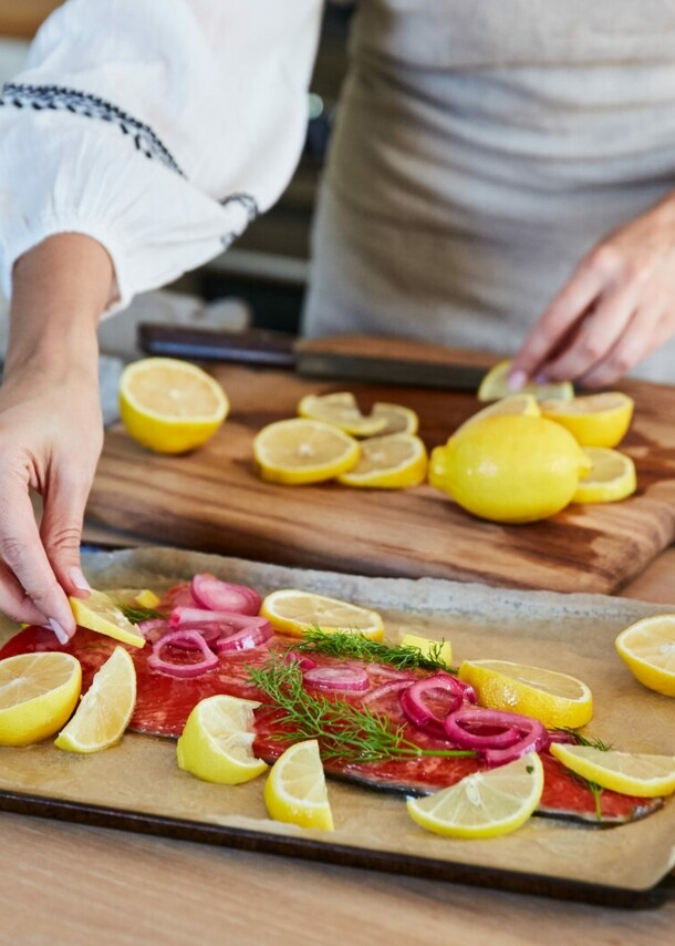 Eine Frau bereitet Lachs mit Zitronenscheiben auf einem Blech in einer Küche zu