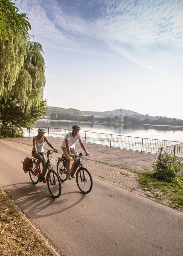 Ein Paar in Sommerkleidung fährt auf Fahrrädern auf einem Radweg entlang eines Flusses
