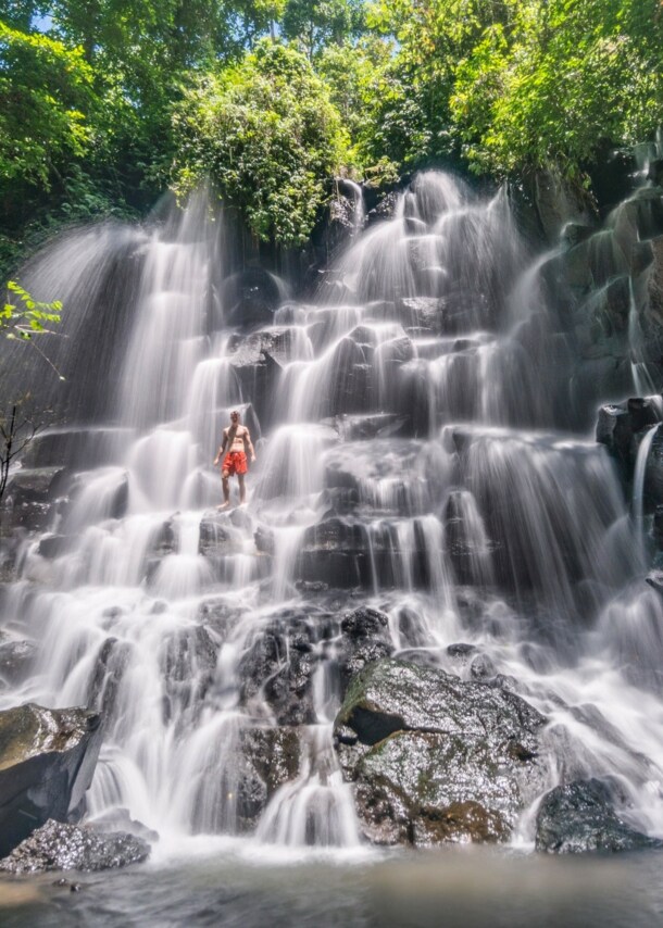 Eine Person in roter Badehose steht in einem gestuften Wasserfall