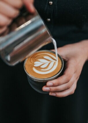 Milchschaum wird in einen Becher Kaffee geschüttet