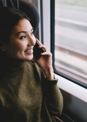 Lächelnde Frau telefoniert in fahrendem Zug und schaut aus dem Fenster