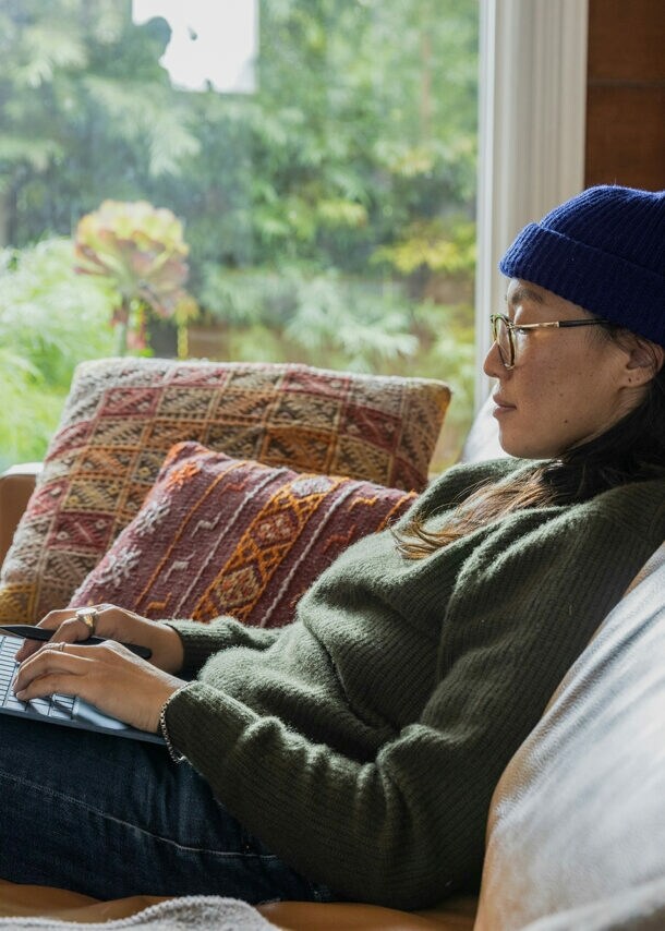 junge Frau sitzt gemütlich mit Laptop auf dem Sofa