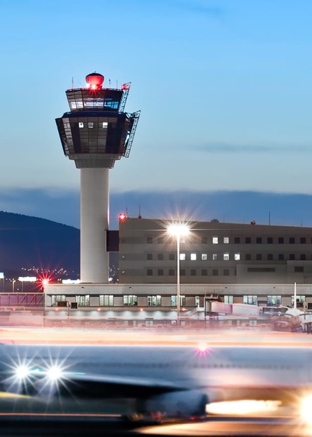 Ein Flugzeug in Bewegungsunschärfe auf dem Rollfeld vor einem Flughafenterminal mit Tower.