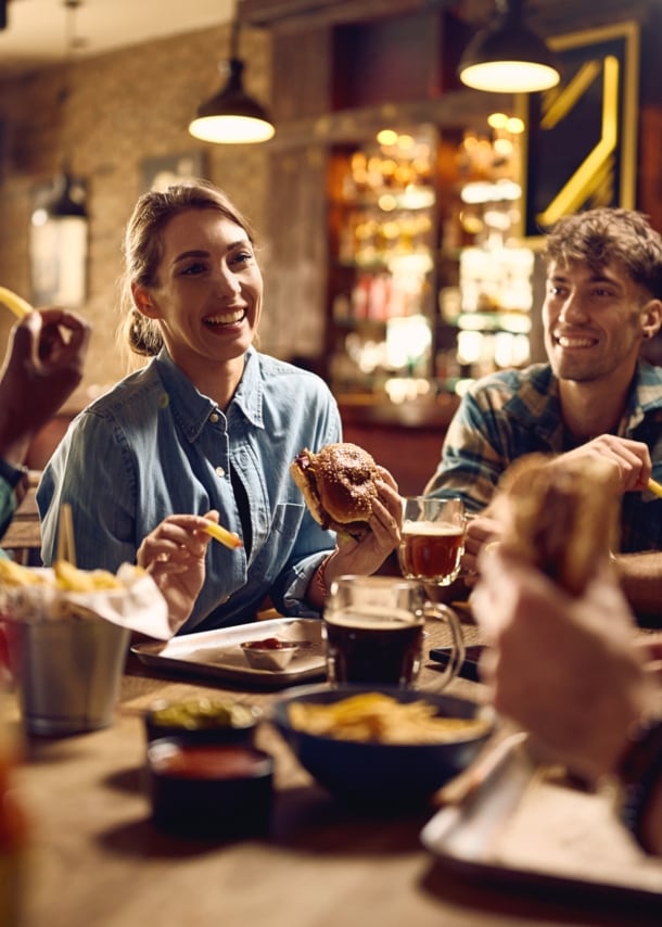 Vier junge Menschen an einem Holztisch essen Fastfood in einem rustikalen Restaurant.