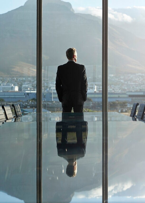 Geschäftsmann blickt aus dem Fenster eines großen Besprechungsraumes auf eine Stadt