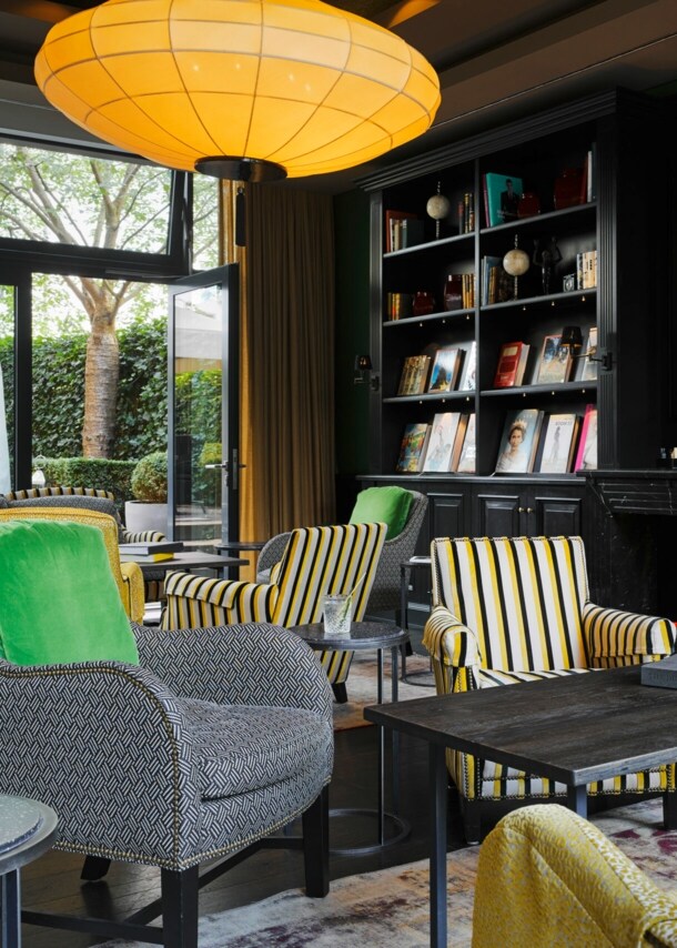Eine gemütlich eingerichtete Hotellobby mit dunkler Schrankwand, Sesseln in Grau- und Gelbtönen und einer großen Glasfront mit Blick auf die Terrasse