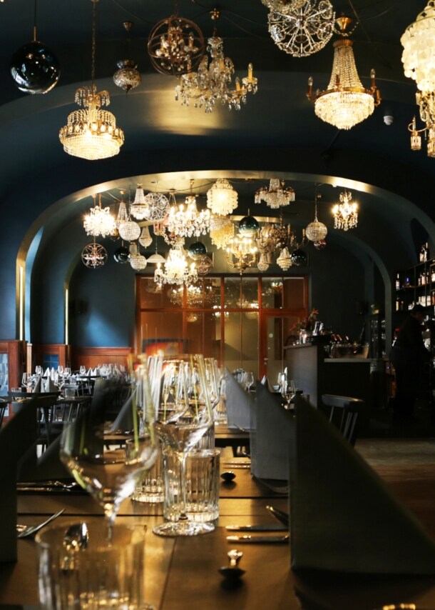 Gastraum des Restaurant AUGUSTIN in Köln mit eingedecktem Tisch im Mittelpunkt und Fokus auf der Deckenbeleuchtung aus vielen verschiedenen Kronleuchtern.
