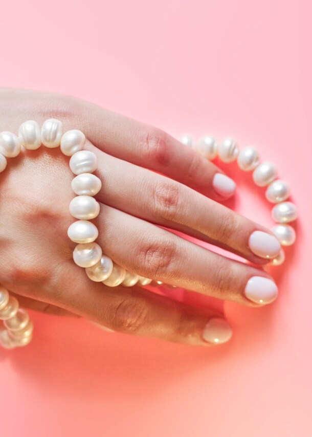 Eine Frauenhand mit Perlenkette umwickelt auf rosa Untergrund