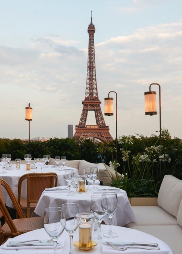 Dachterrasse eines Restaurants mit weiß eingedeckten Tischen vor dem Eiffelturm.