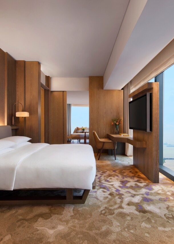 Moderne Hotelsuite mit Holzelementen und Aussicht auf das Hafengebiet von Singapur durch raumhohe Panoramafenster.
