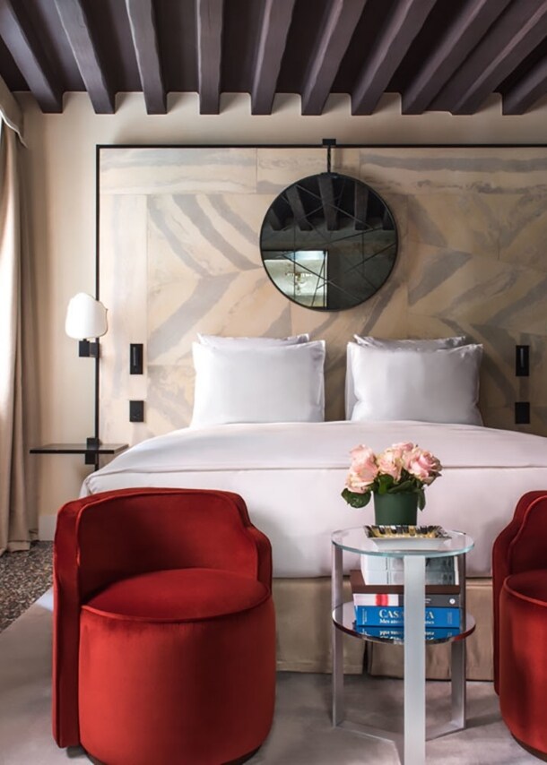 Stilvolles Hotelzimmer mit Doppelbett, im Vordergrund eine geöffnete Flügeltür mit goldenen Türklinken.
