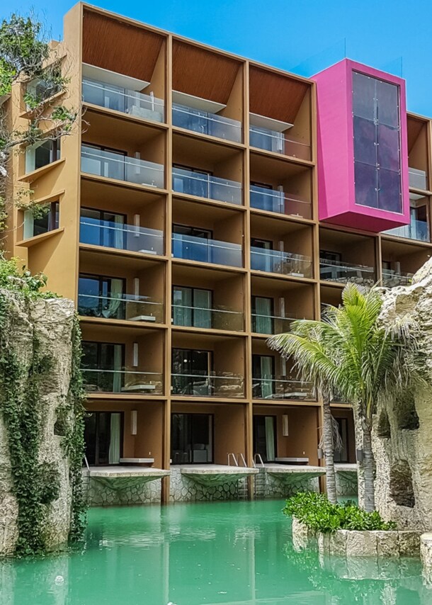 Moderner Hotelkomplex, umgeben von bepflanzten Felsen an einem Pool mit türkisfarbenem Wasser.