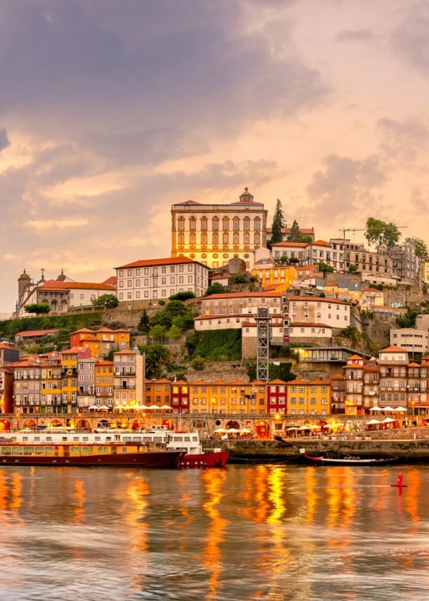 Panoramaaufnahme der Stadt Porto bei Sonnenuntergang mit dem Fluss Duoro im Vordergrund.