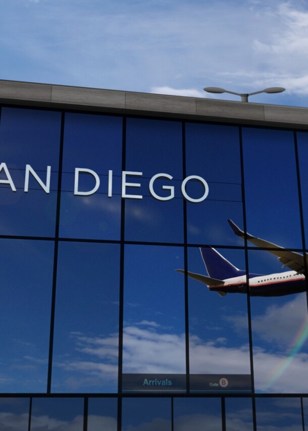 Flugzeug beim Abflug, das sich in den verspiegelten Fenstern einer Flughafenhalle spiegelt, auf denen die Aufschrift „San Diego“ zu lesen ist.