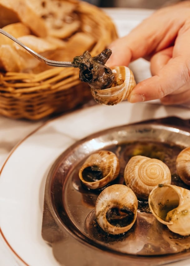 Nahaufnahme von zwei Händen beim Essen von Weinbergschnecken auf einem Teller in einer Brasserie.