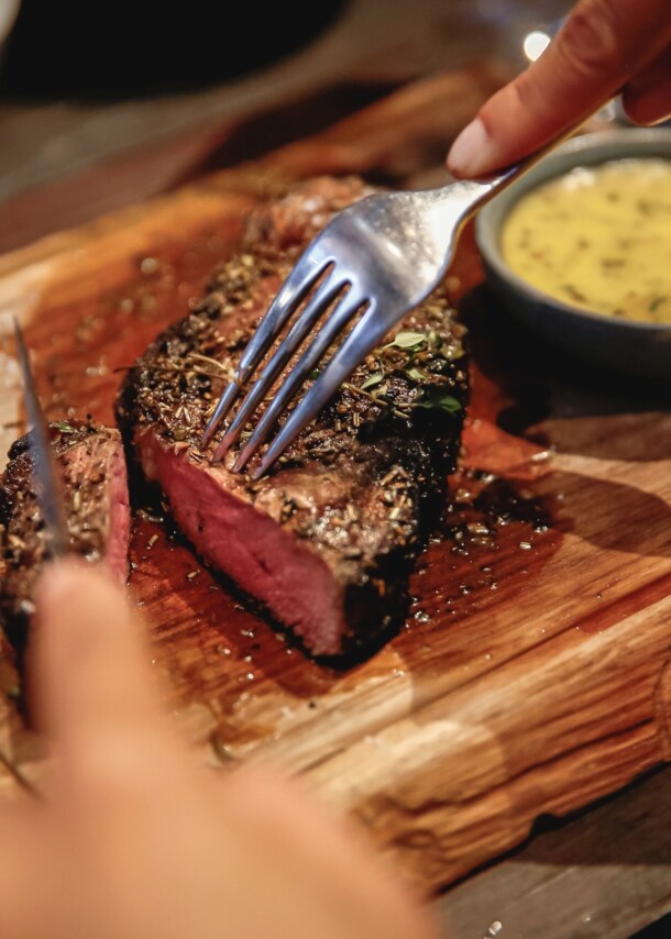 Nahaufnahme eines angeschnittenen Steaks auf einem Holzbrett neben einer Schale mit Soße.