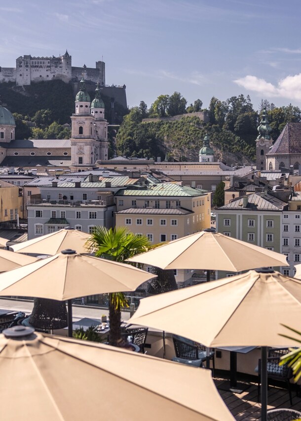 Panorama der Salzburger Altstadt mit Burg auf einem Berg am Fluss, im Hotelterrasse mit Sonnenschirmen.